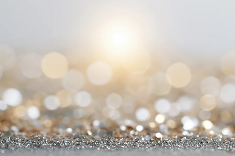 Scattered silver and gold glitter on a surface with defocused bokeh lights in the background
