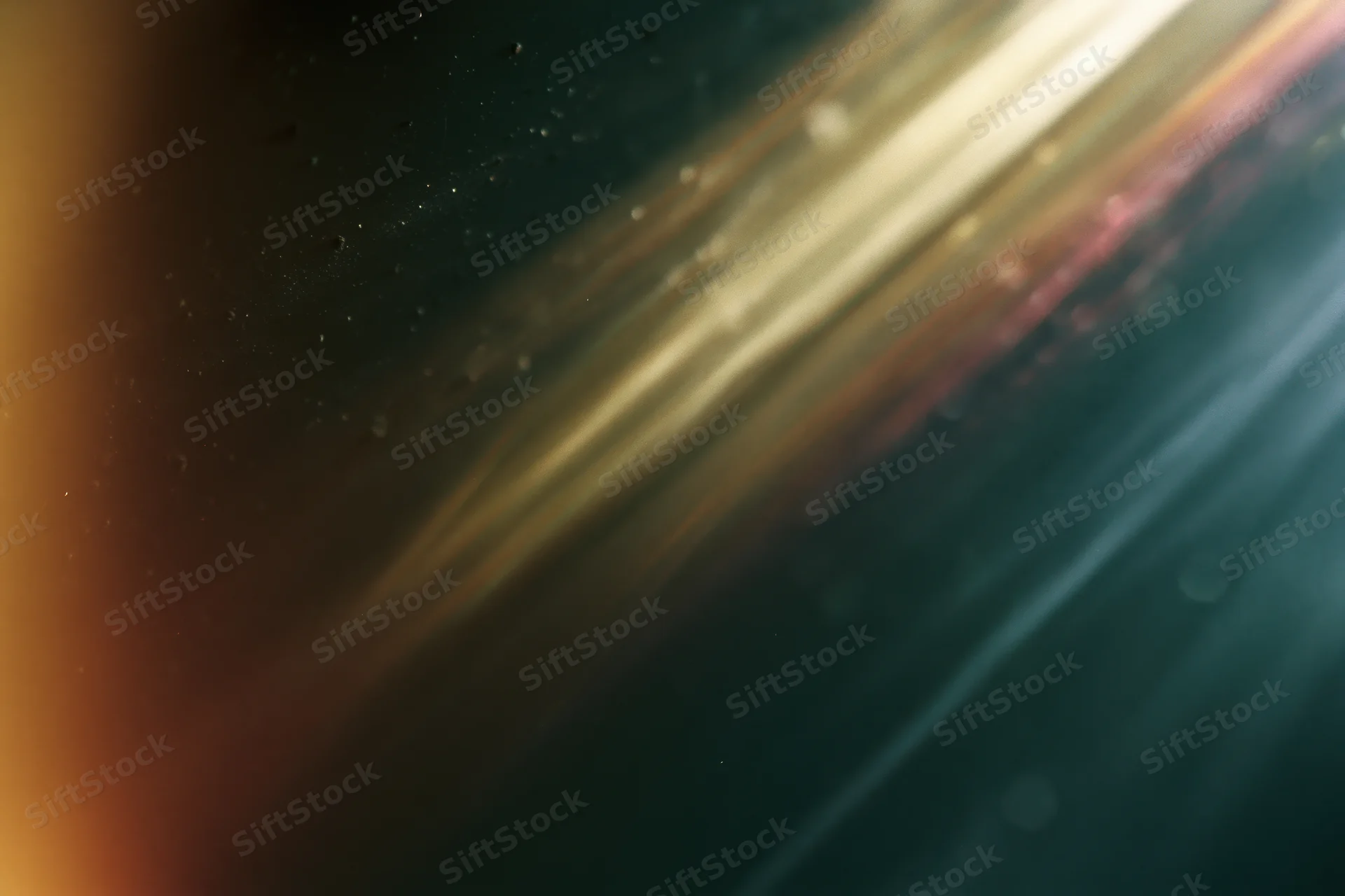 Diagonal light leak glowing across a dark dusty surface with scattered particles and soft bokeh highlights