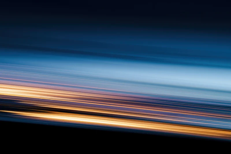 Horizontal light streaks from moving vehicles at night creating abstract motion blur background