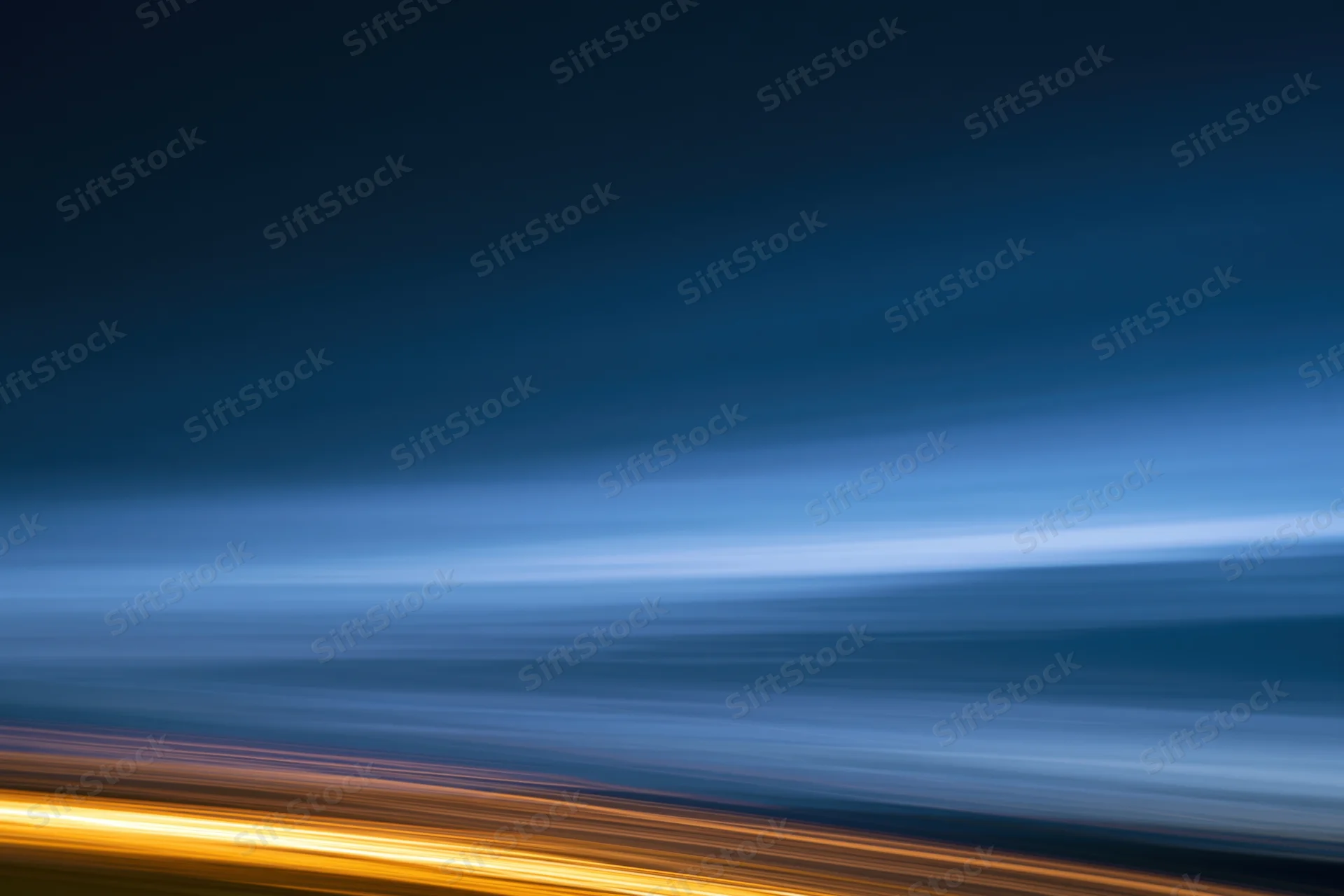 Horizontal light streaks from moving vehicles at night against a dark blue sky gradient