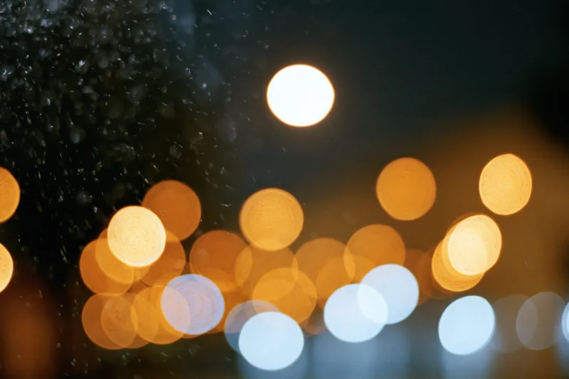 Warm and white circular bokeh lights blurred in a dark urban night scene with rain droplets on a surface