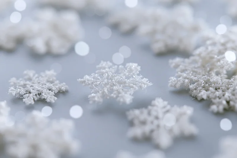 White snowflakes scattered on a soft gray surface with bokeh lights in the background