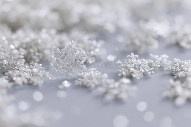 Scattered silver snowflakes with bokeh lights on a soft white surface