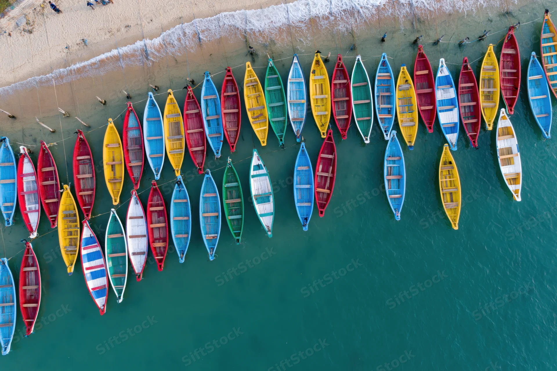 Colorful traditional boats moored in rows along a sandy beach in turquoise water