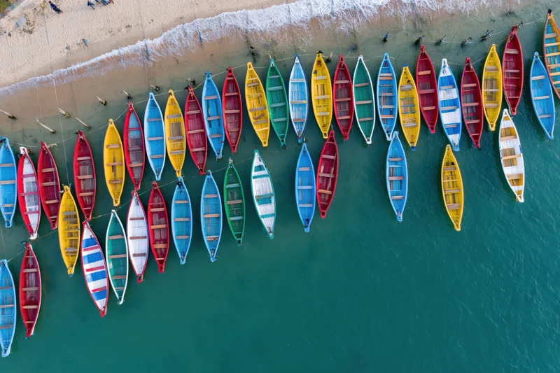 Colorful traditional boats moored in rows along a sandy beach in turquoise water