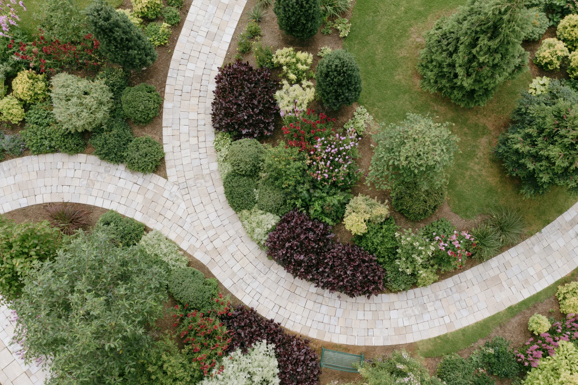 Aerial top-down view of a manicured residential garden with curved stone pathways and colorful shrubs and flowering plants arranged in landscaped beds