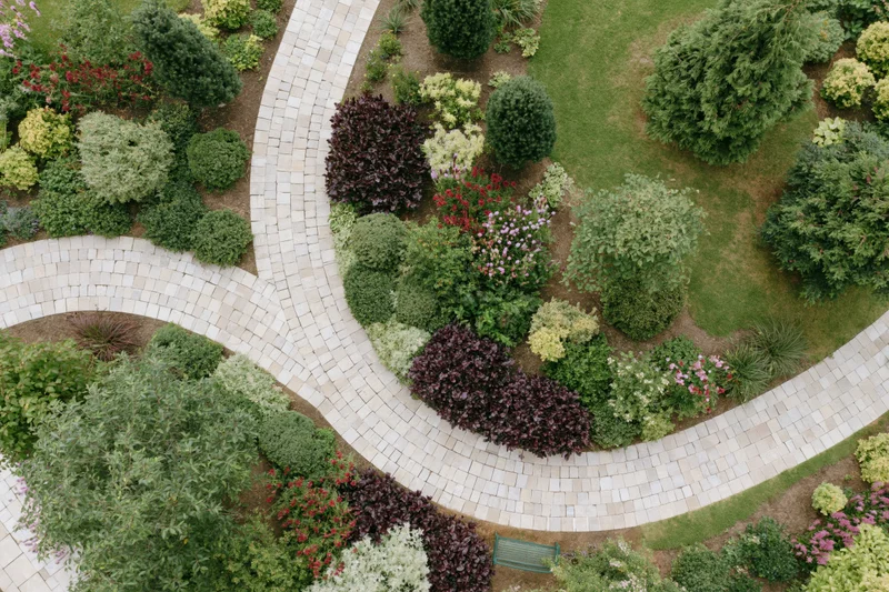 Aerial top-down view of a manicured residential garden with curved stone pathways and colorful shrubs and flowering plants arranged in landscaped beds