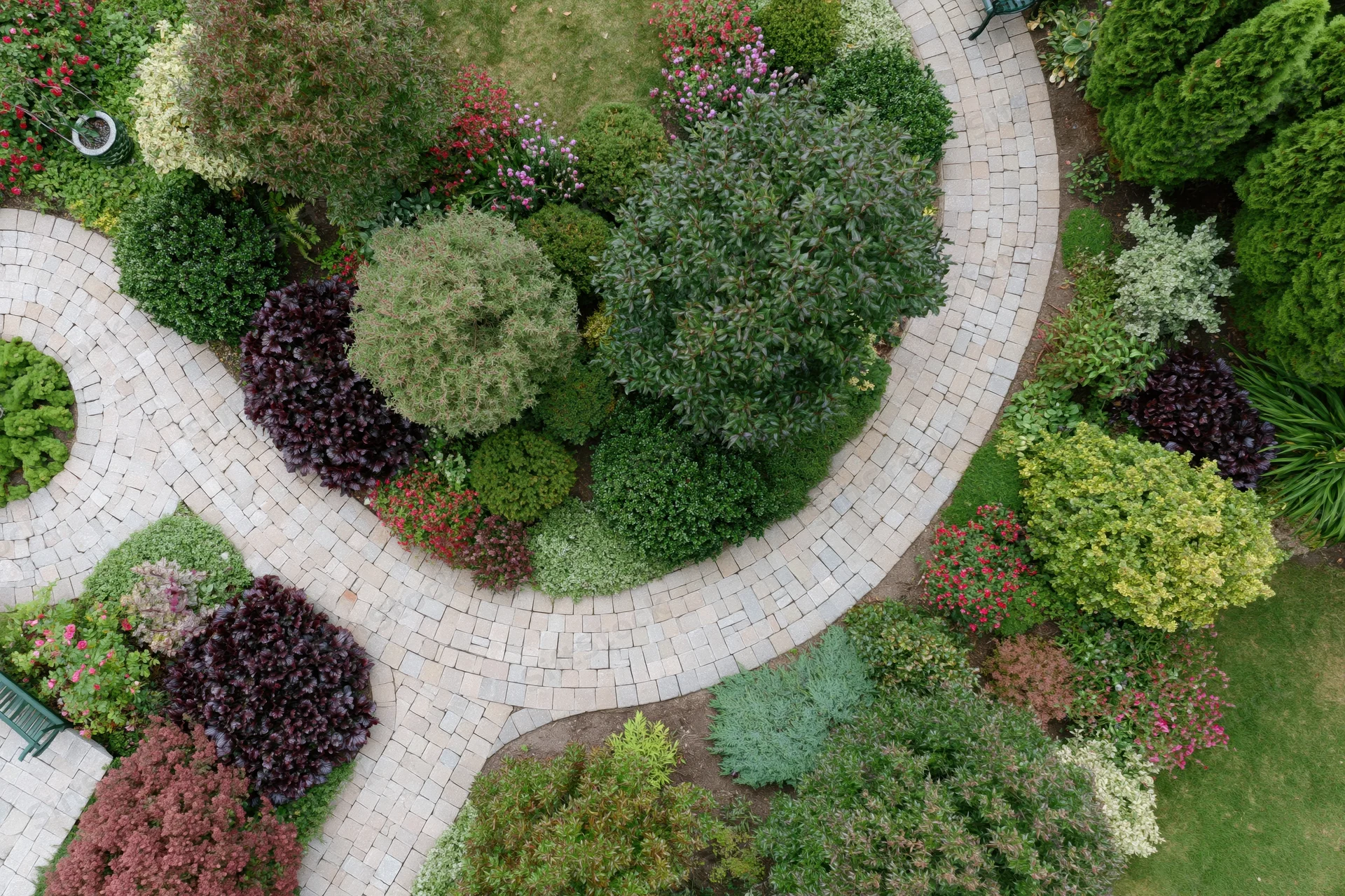 Aerial top-down view of a manicured residential garden with curved stone pathways and colorful shrubs and flowers arranged in borders