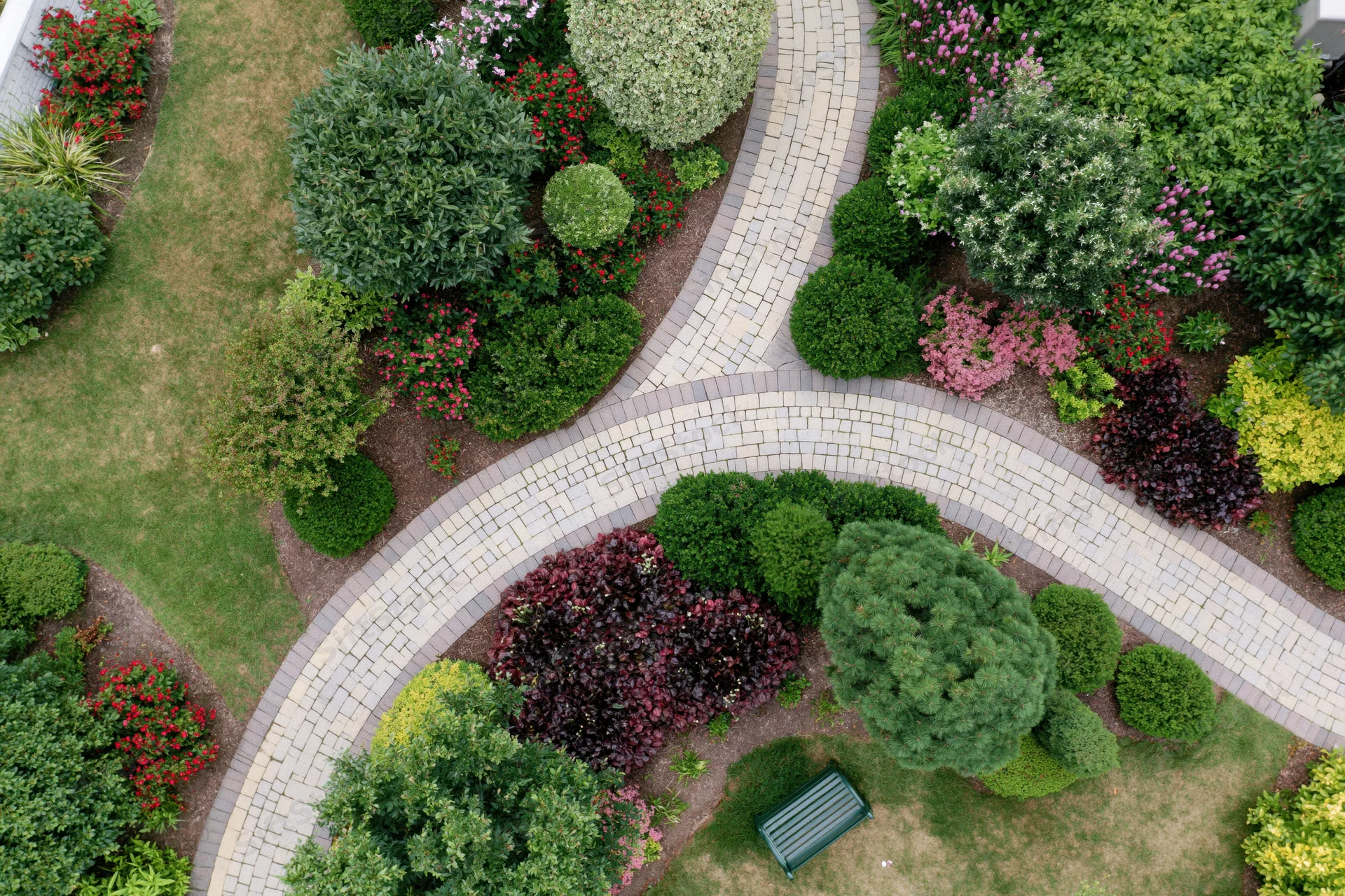 Aerial top-down view of a manicured residential garden with curved stone pathways and colorful shrubs and flowers