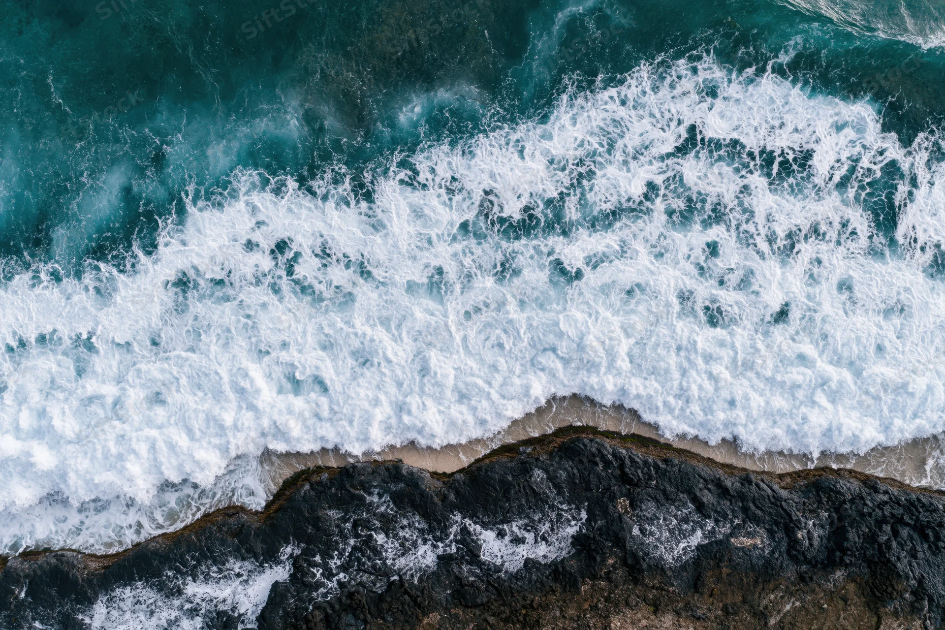 Ocean waves breaking over rocky coastline from aerial top-down view