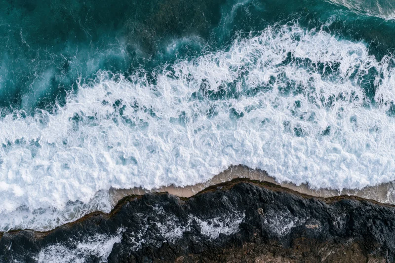 Ocean waves breaking over rocky coastline from aerial top-down view