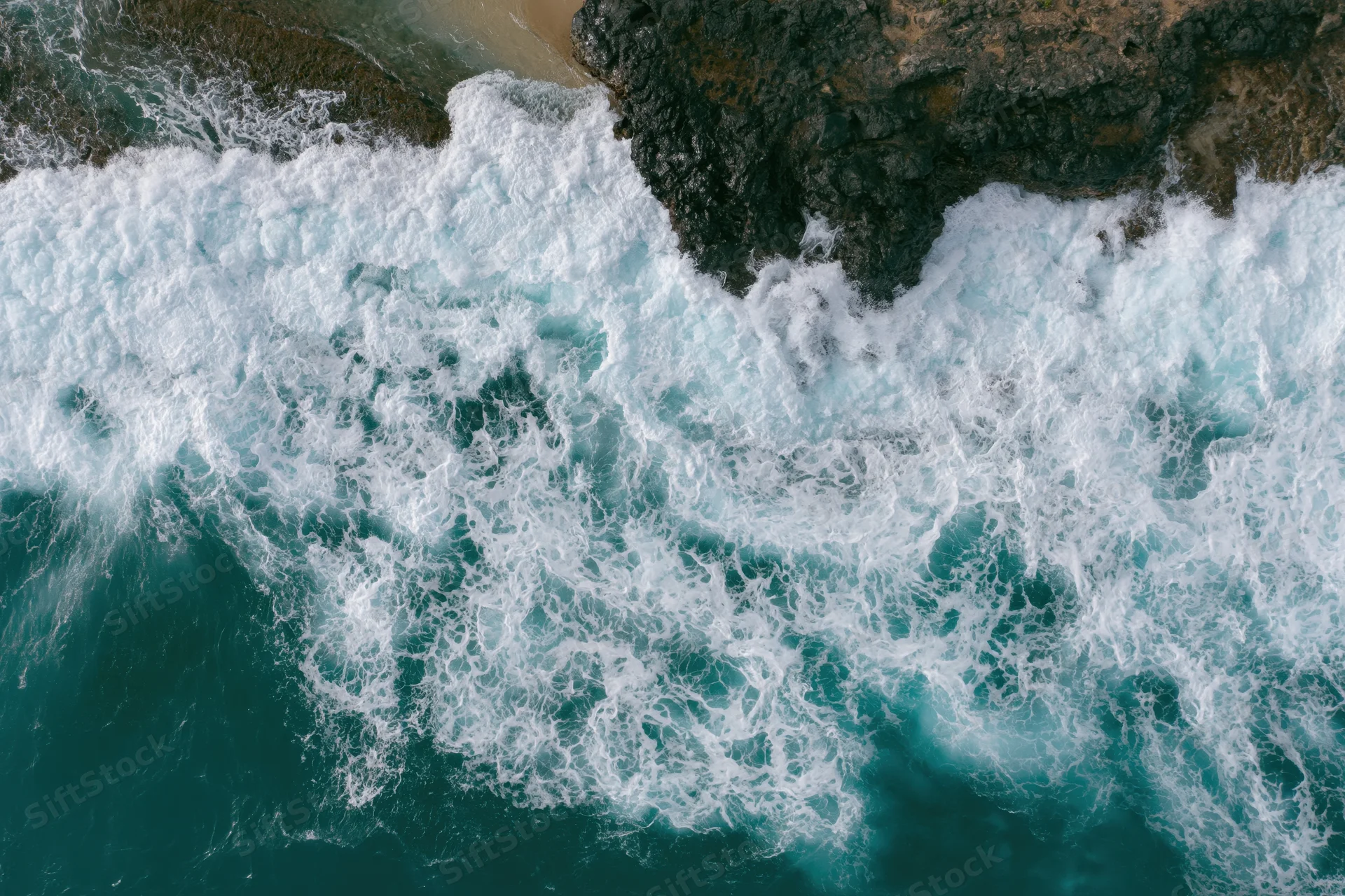 Ocean waves breaking over rocky coastline from aerial top-down view
