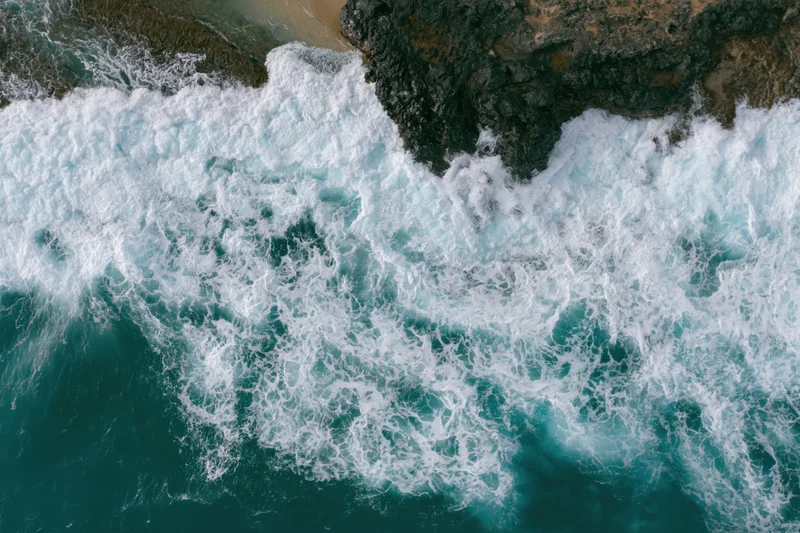 Ocean waves breaking over rocky coastline from aerial top-down view