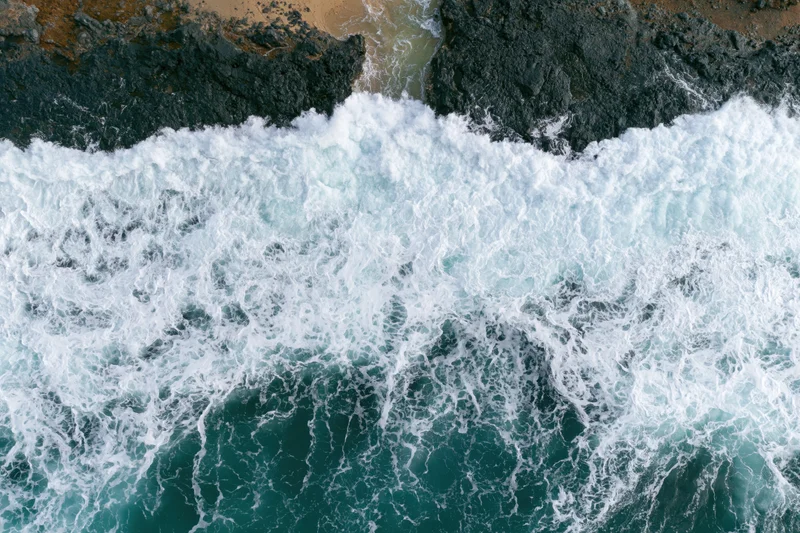 Ocean waves breaking over rocky coastline from aerial top-down view