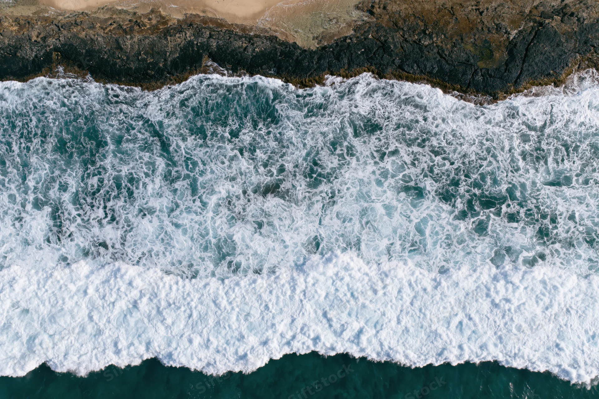 Ocean waves breaking over rocky coastline from aerial top-down view