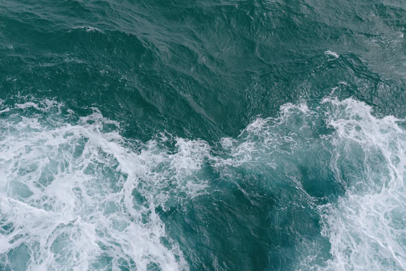 Aerial top-down view of ocean surface with small ripples and breaking waves creating white foam