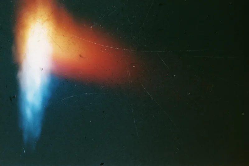 Light leak artifact on aged film scan showing orange and blue glow against dark background with scratches and dust