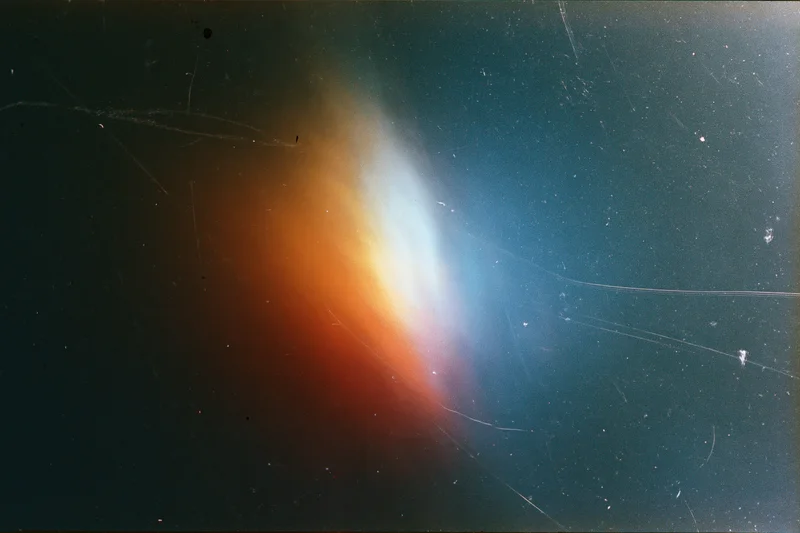 Light leak artifact in aged film scan showing orange and blue gradient glow against dark space background