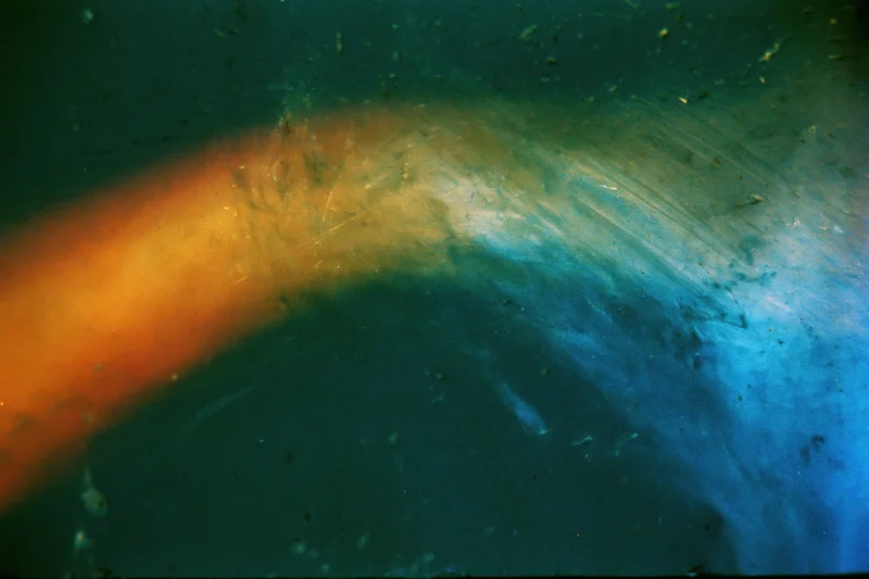Aged film scan showing light leak and lens flare with orange and blue color gradient