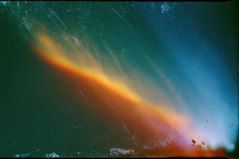 Aged film scan showing light leak and lens flare with color gradients and surface scratches