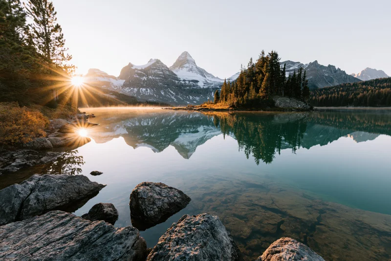 Alpine lake reflecting snow-capped mountains and pine-covered island at sunrise