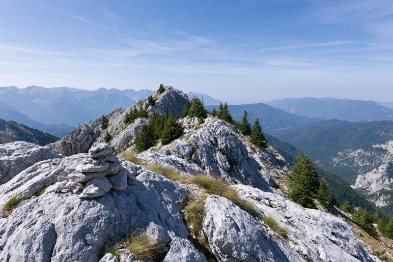 Stone cairn on rocky alpine ridge with distant mountain range in background