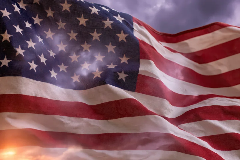 American flag rippling in wind against cloudy sky with sunrise glow
