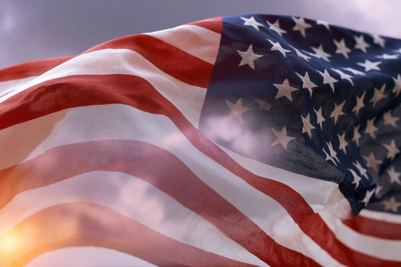 American flag rippling in wind filling the frame with stars and stripes against sky and sunlight