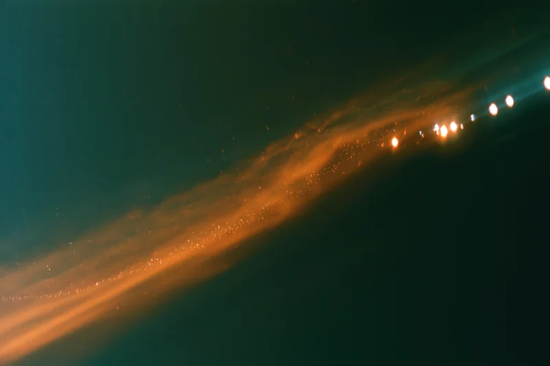 Diagonal streak of warm glowing light with bokeh flares on dark analog film background