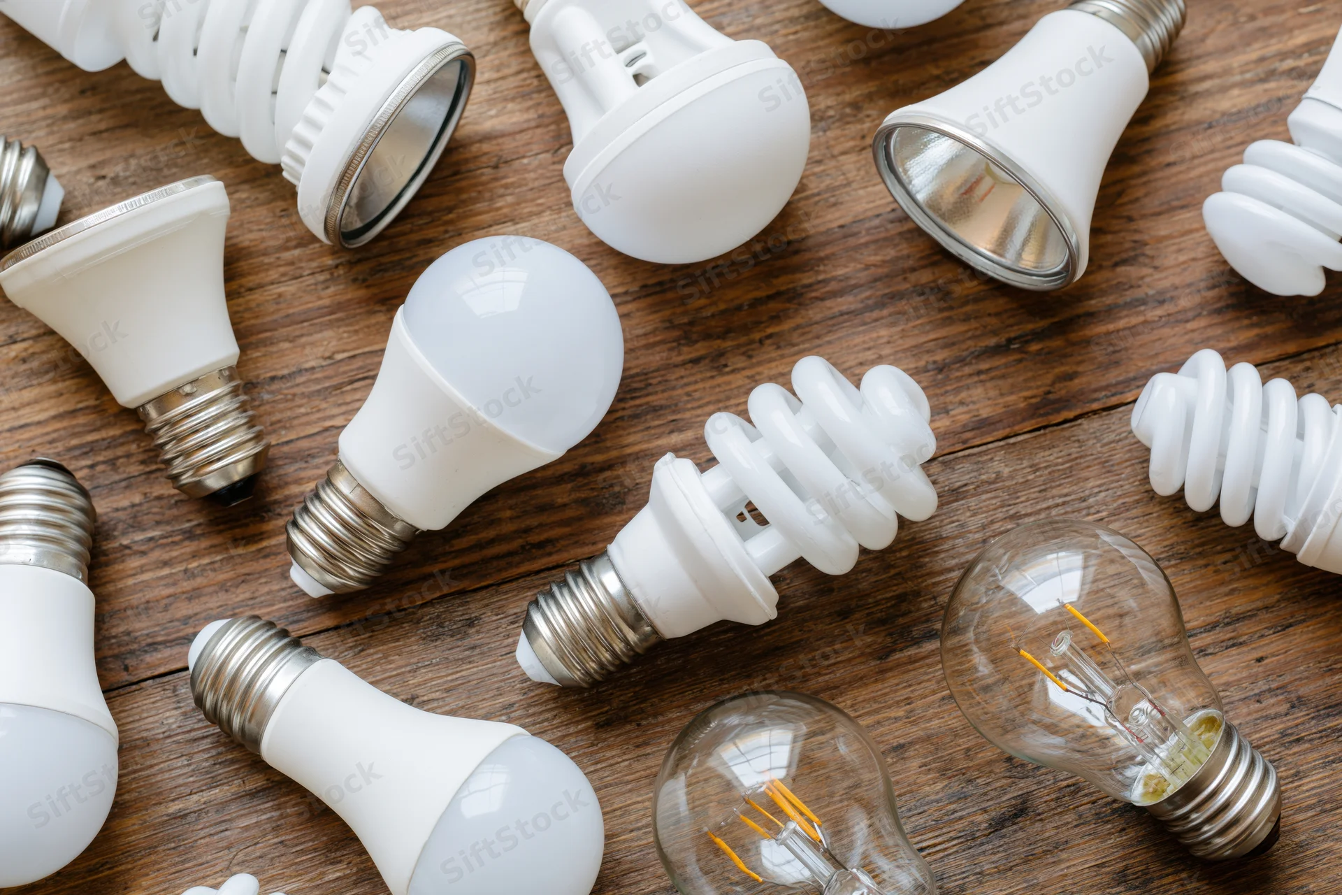 Assorted light bulbs of various types scattered on a wooden table surface