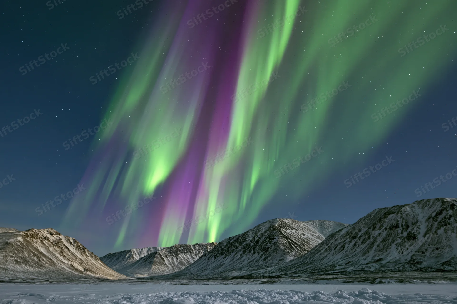 Aurora borealis glowing in green and purple over snow-covered mountains at night
