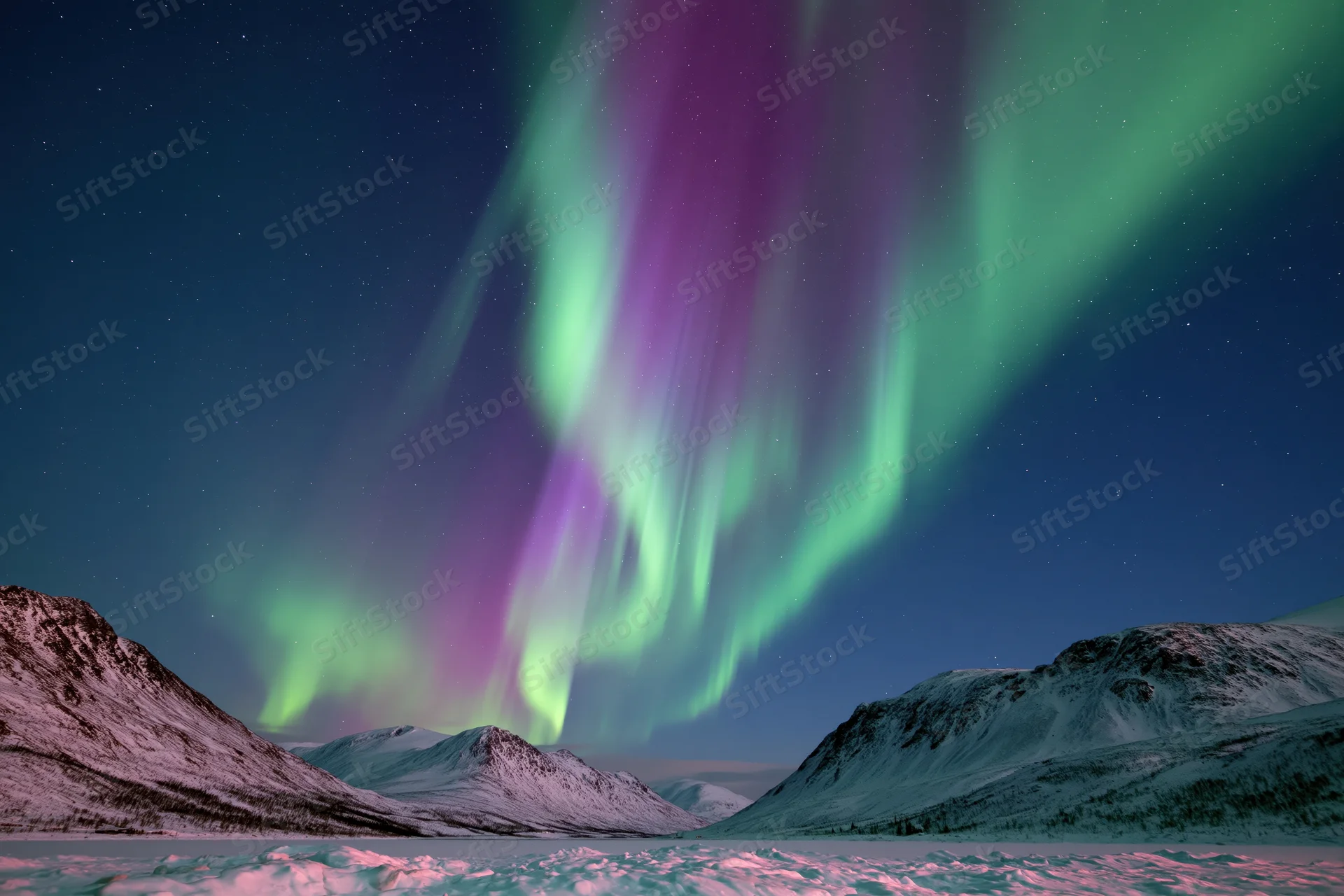 Aurora borealis glowing in green and purple over snow-covered mountains and frozen lake at night