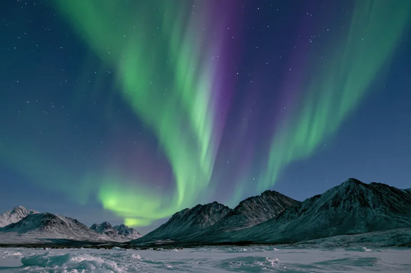 Aurora borealis glowing over snow-covered mountains in a frozen arctic landscape at night