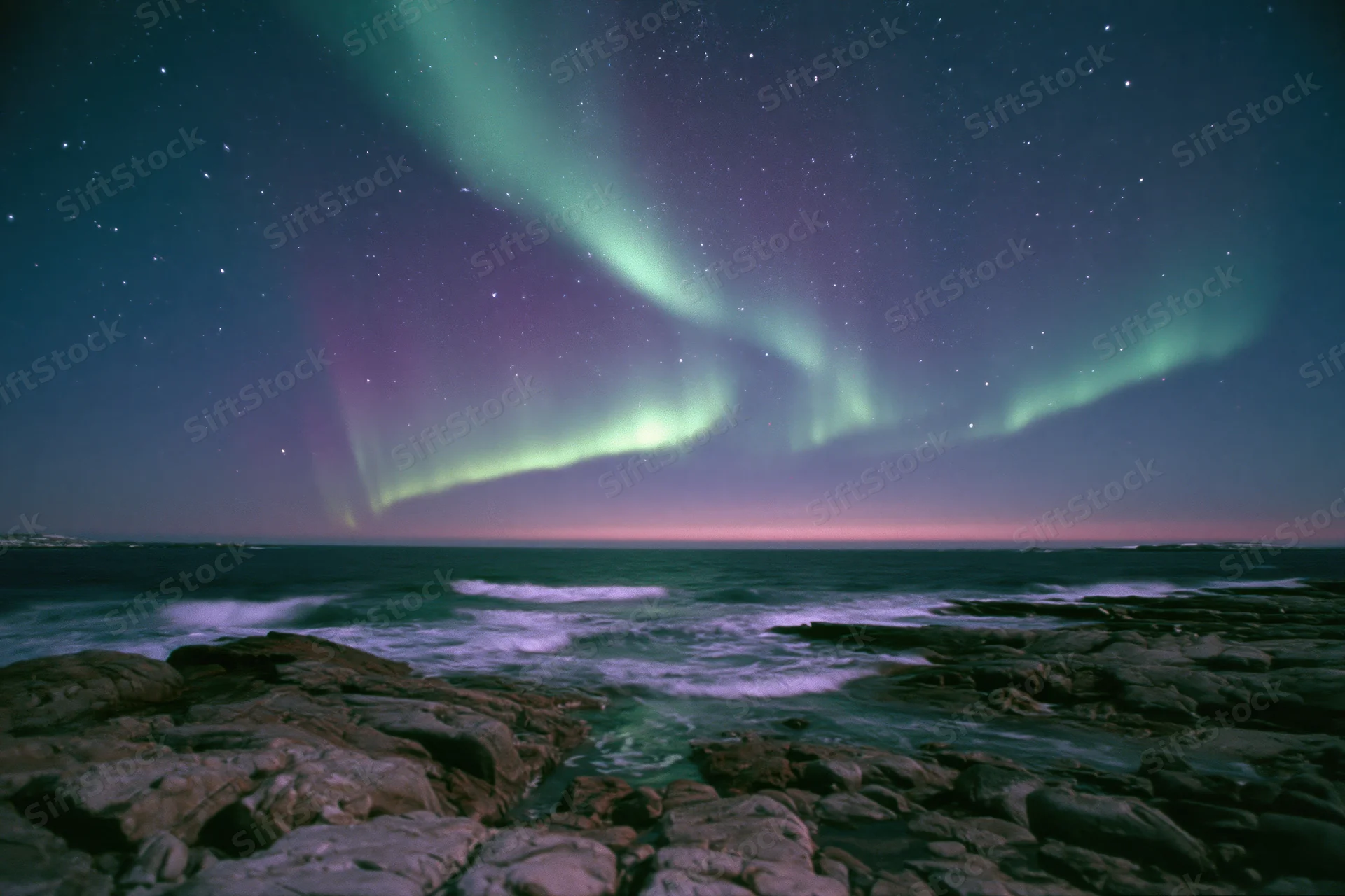 Aurora borealis sweeping across night sky over rocky coastline with ocean waves
