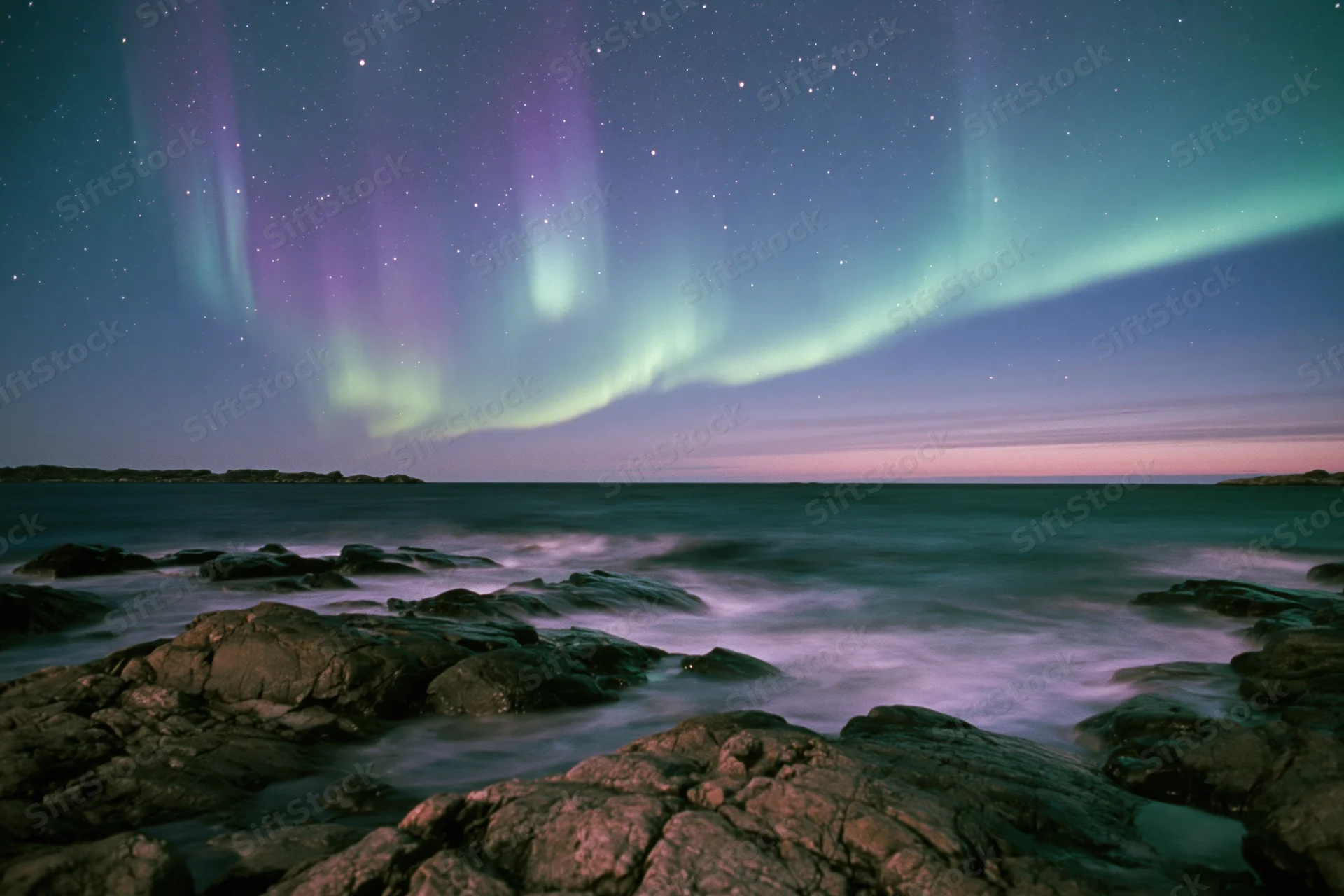 Aurora borealis sweeping across night sky over rocky coastline with ocean waves