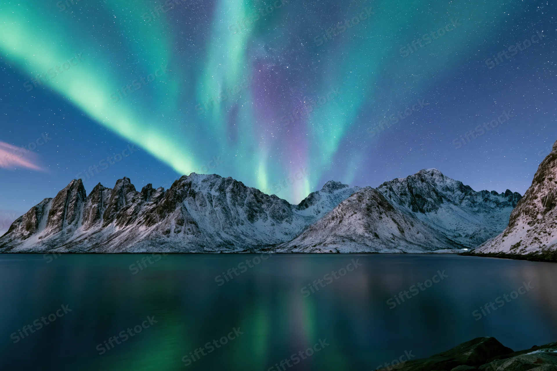 Aurora borealis sweeping over snow-covered mountains reflected in calm lake water