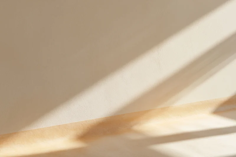 Beige plaster wall meeting smooth wooden floor with sunlight and shadows in empty interior