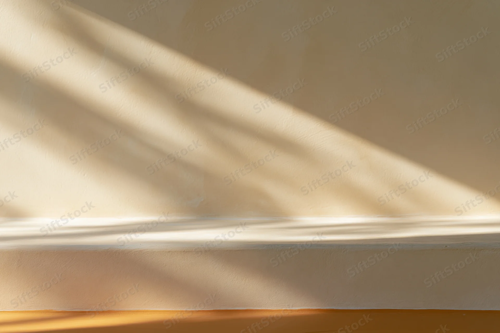 Beige plaster wall meeting smooth surface below with sunlight and shadows