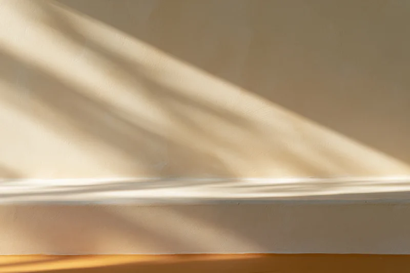 Beige plaster wall meeting smooth surface below with sunlight and shadows