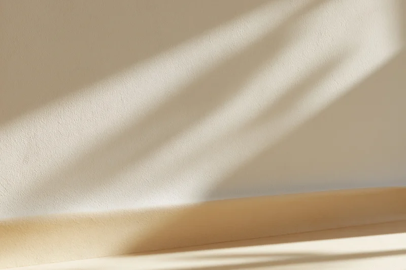 Beige plaster wall meeting smooth surface below with sunlight casting diagonal shadows