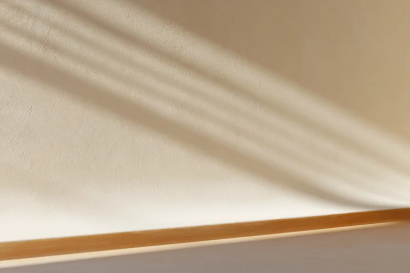 Beige plaster wall meeting smooth surface below with shadow stripes and wooden trim
