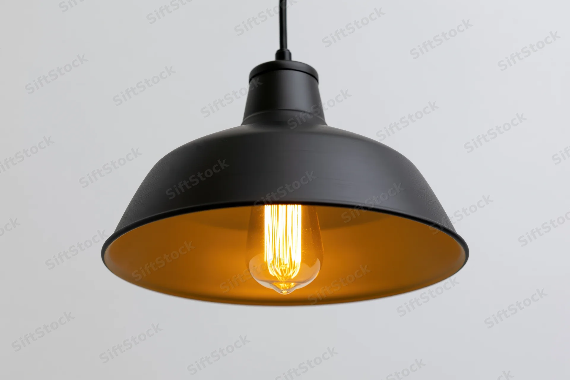 Black matte metal industrial pendant lamp hanging from ceiling with glowing edison bulb inside warm-toned shade