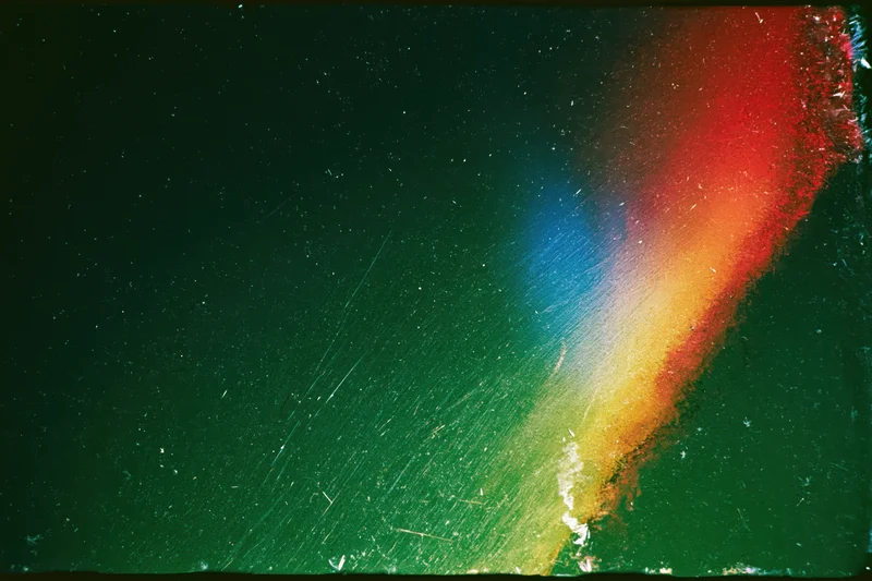 Damaged 35mm film frame with colorful light leak streaks across dark green background