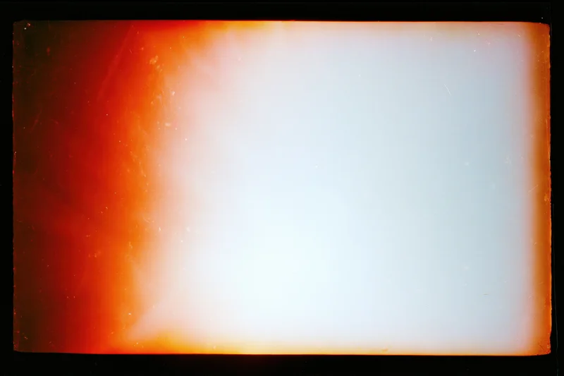 Blank overexposed analog film frame with heavy light leak bleeding from edges into white center