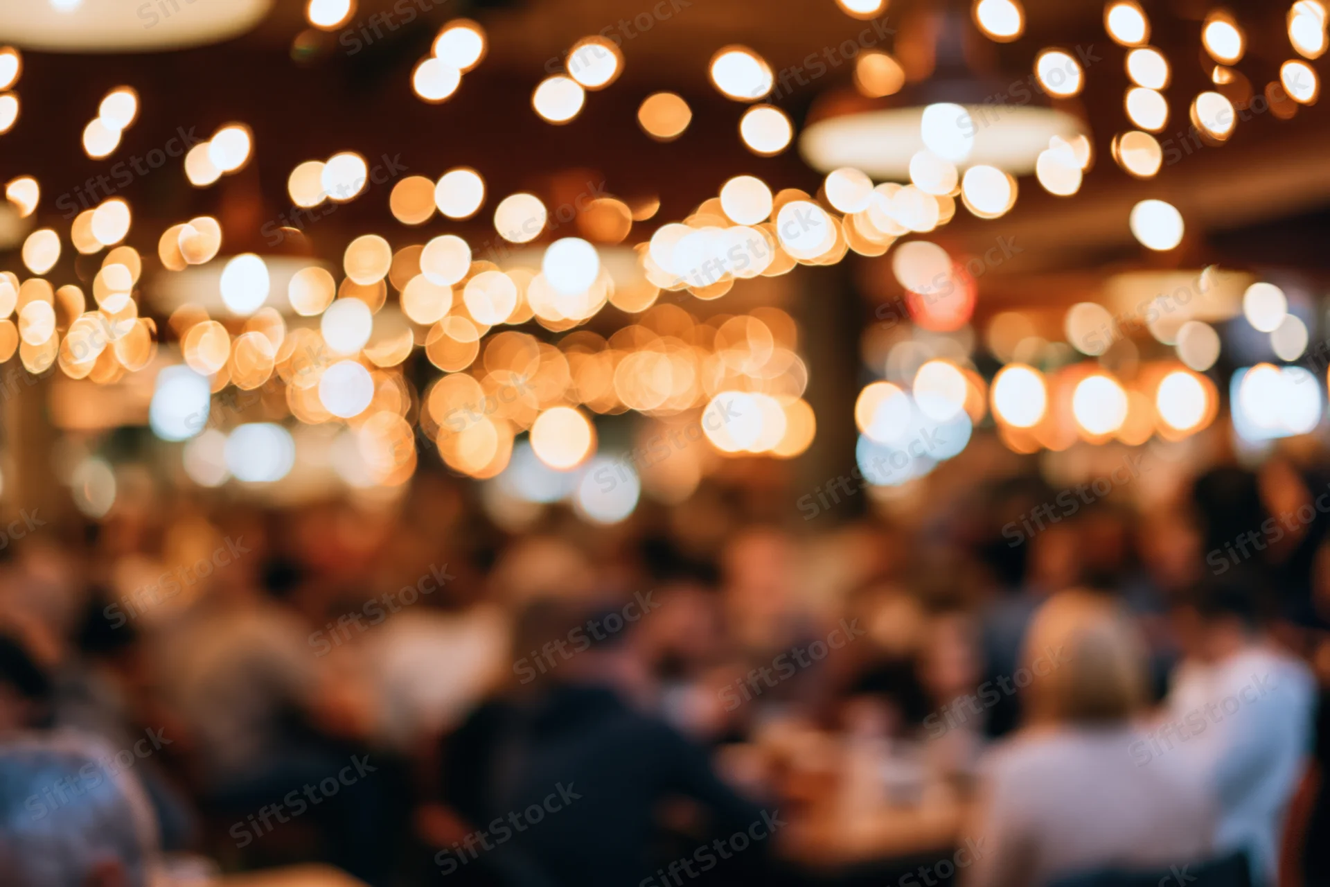 Blurred view of a crowded restaurant interior at night with warm bokeh lights overhead