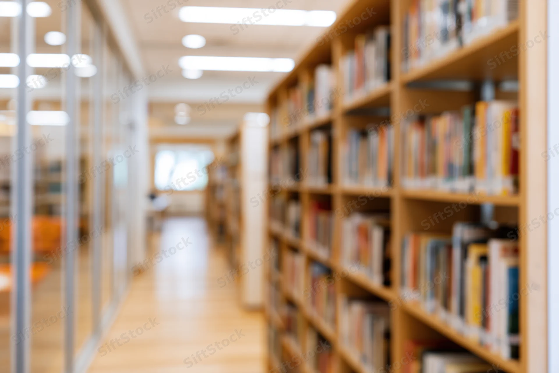 Blurred library aisle with bookshelves lining wooden floor leading toward bright light