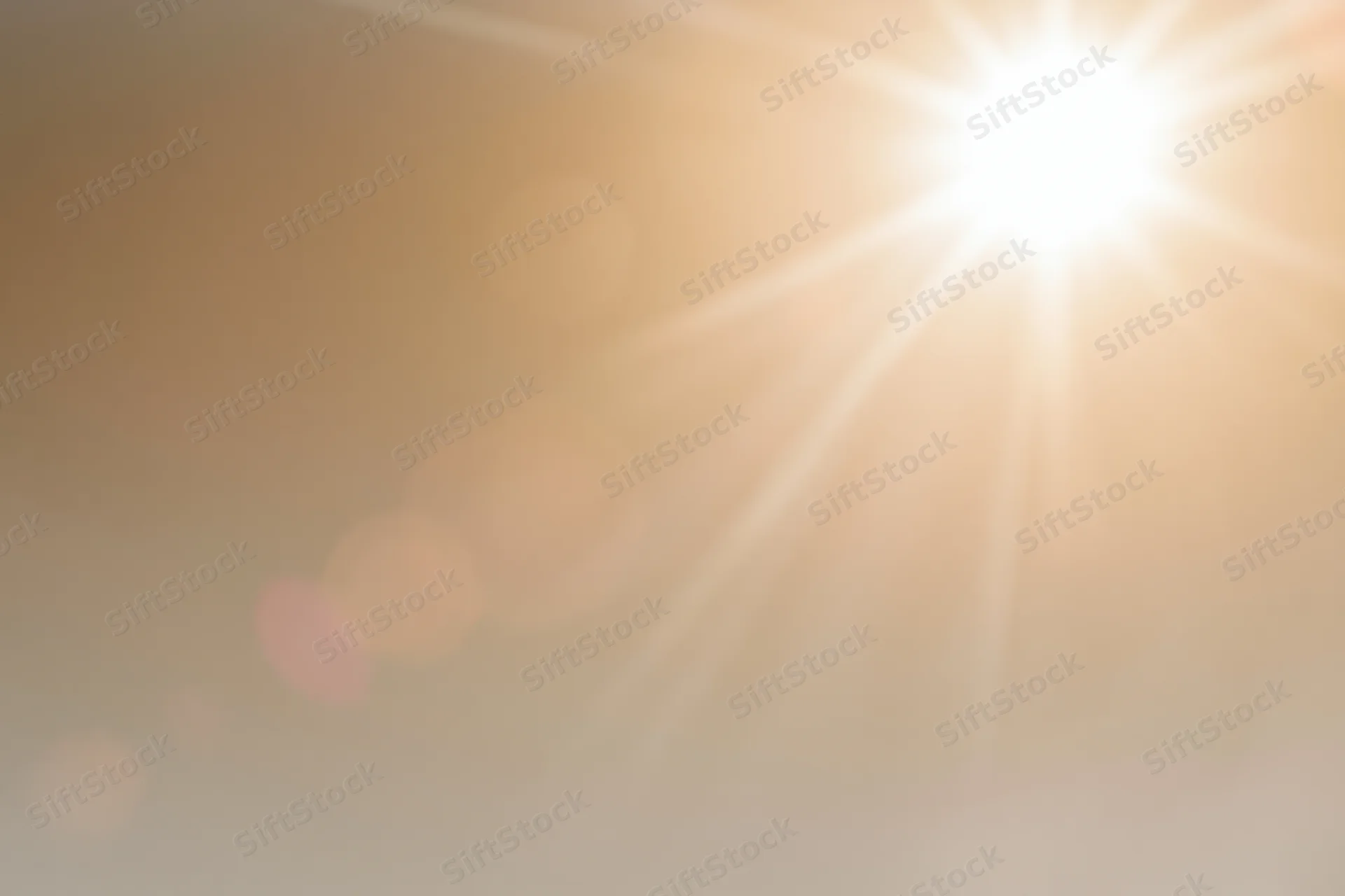 Bright midday sun bursting from upper right corner against hazy sky with lens flare and bokeh highlights