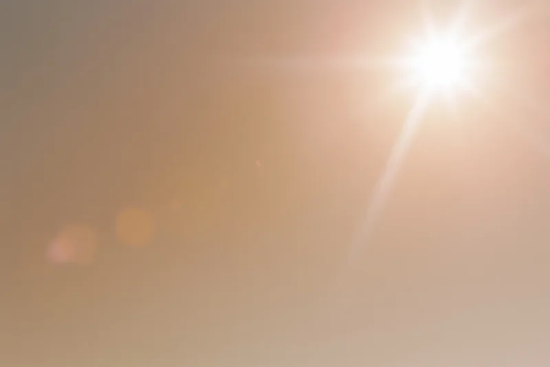 Bright midday sun bursting from upper right corner against hazy sky