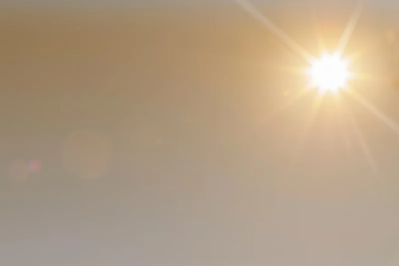 Bright midday sun bursting from the upper right corner against a hazy golden sky