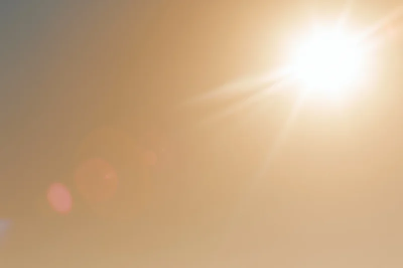 Bright midday sun bursting from upper right corner against hazy sky with lens flare and bokeh highlights